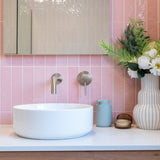 a brushed nickel wall mixer and spout on a pink tiled background