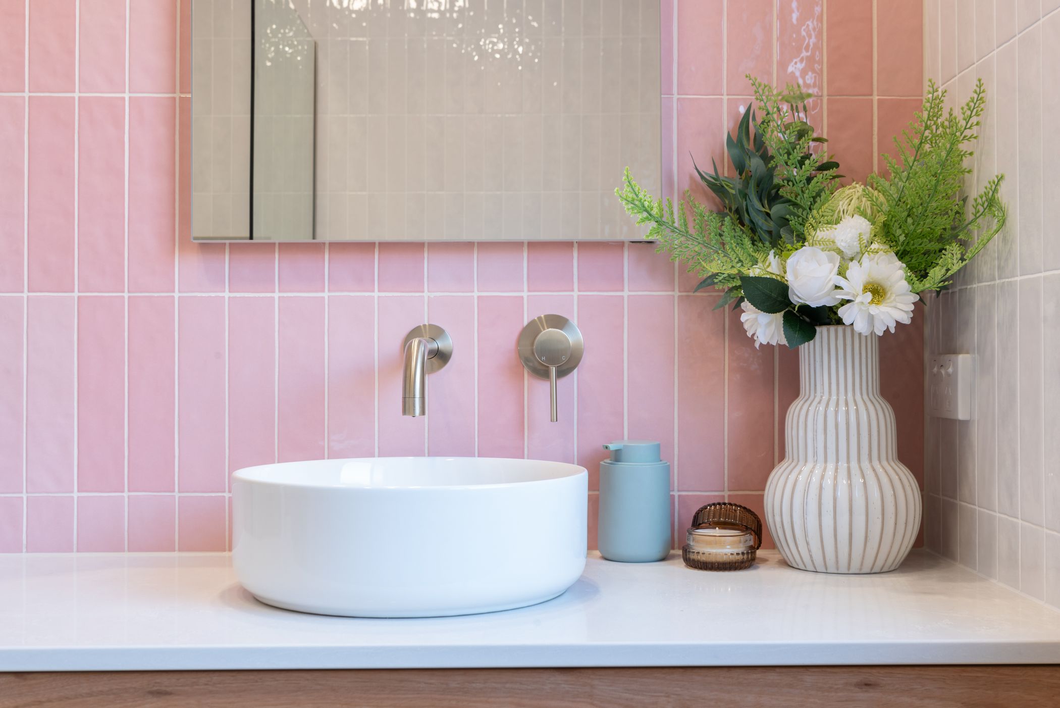a brushed nickel wall mixer and spout on a pink tiled background