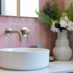 a brushed nickel wall spout and mixer wall mounted on a pink tiled background and a white basin
