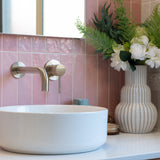 a brushed nickel wall spout and mixer wall mounted on a pink tiled background and a white basin