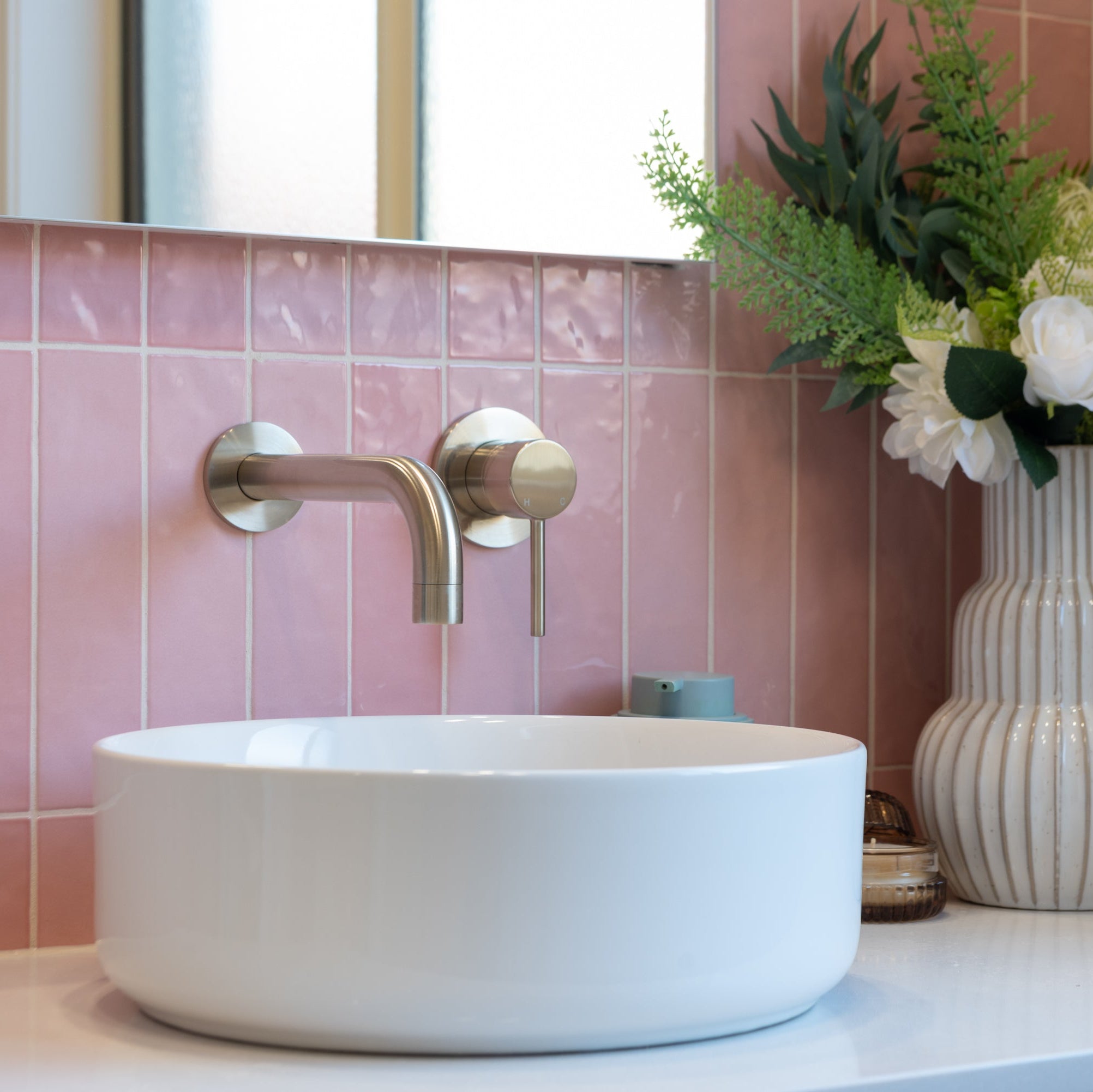 a brushed nickel wall spout and mixer wall mounted on a pink tiled background and a white basin