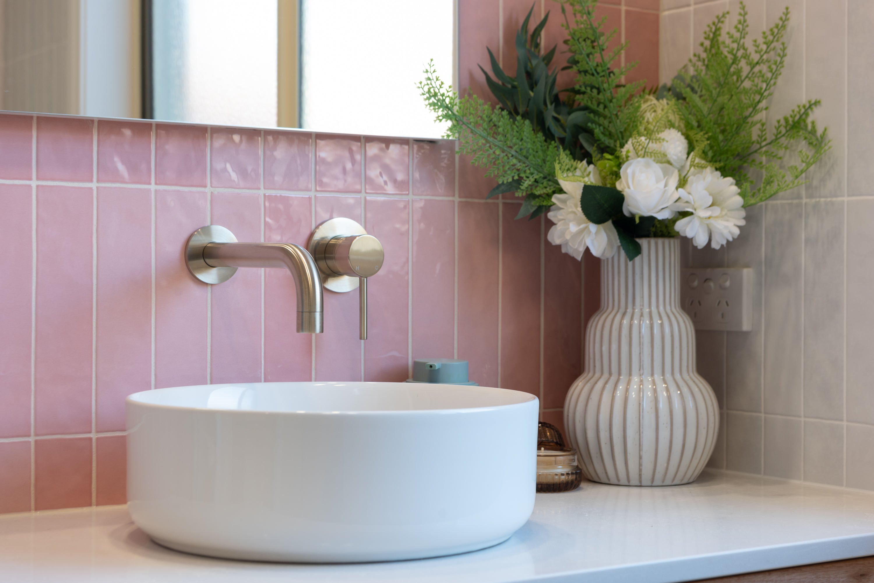 a brushed nickel wall spout and mixer wall mounted on a pink tiled background and a white basin