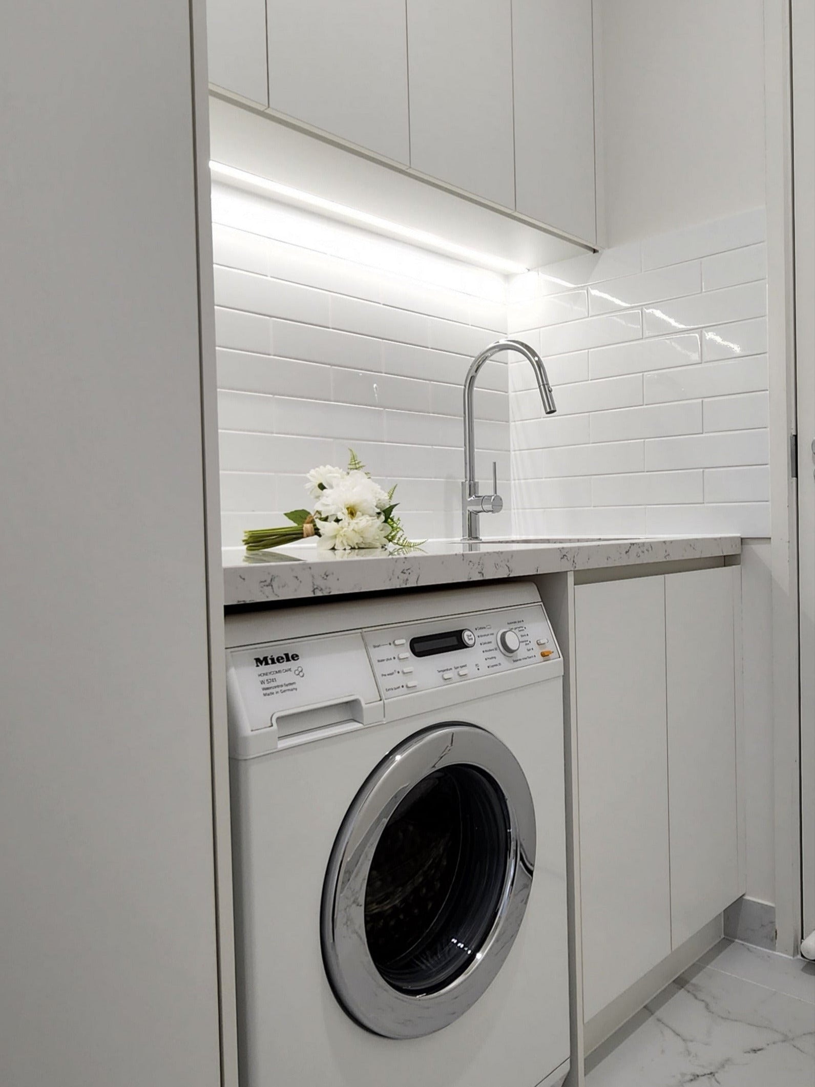 Modern laundry with white cabinets, white splashback and chrome pull-out kitchen/laundry mixer