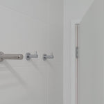 Bathroom corner with a chrome towel rack and robe hooks on a white tiled wall.