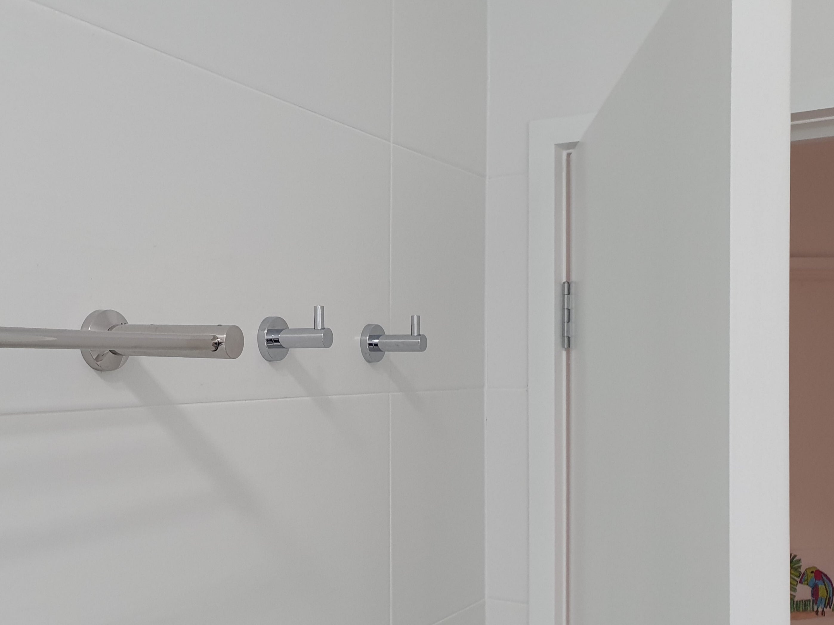 Bathroom corner with a chrome towel rack and robe hooks on a white tiled wall.