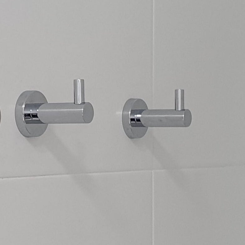Bathroom corner with a chrome towel rack and robe hooks on a white tiled wall.