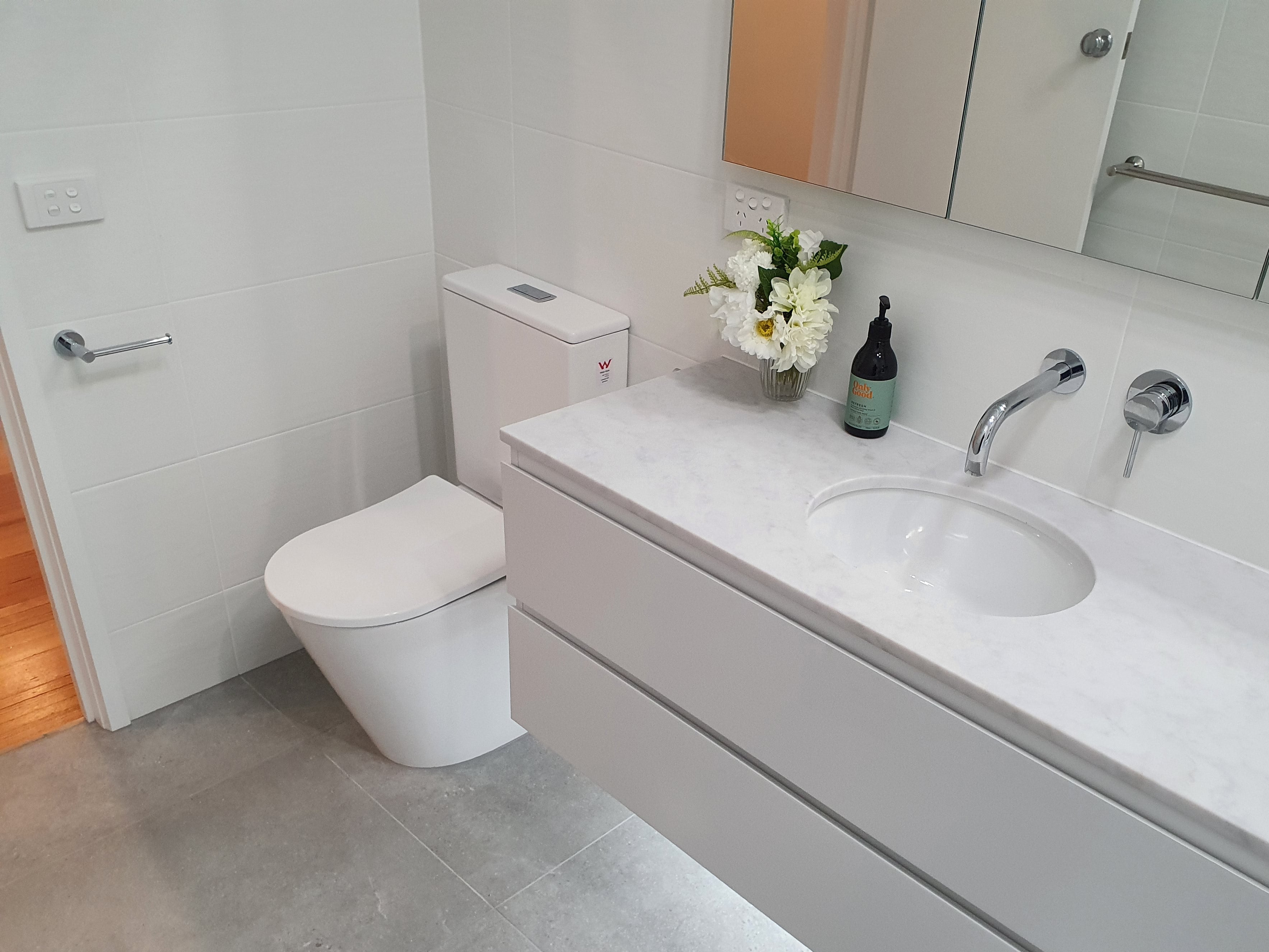 Modern bathroom with toilet, sink, vanity and chrome toilet roll holder.
