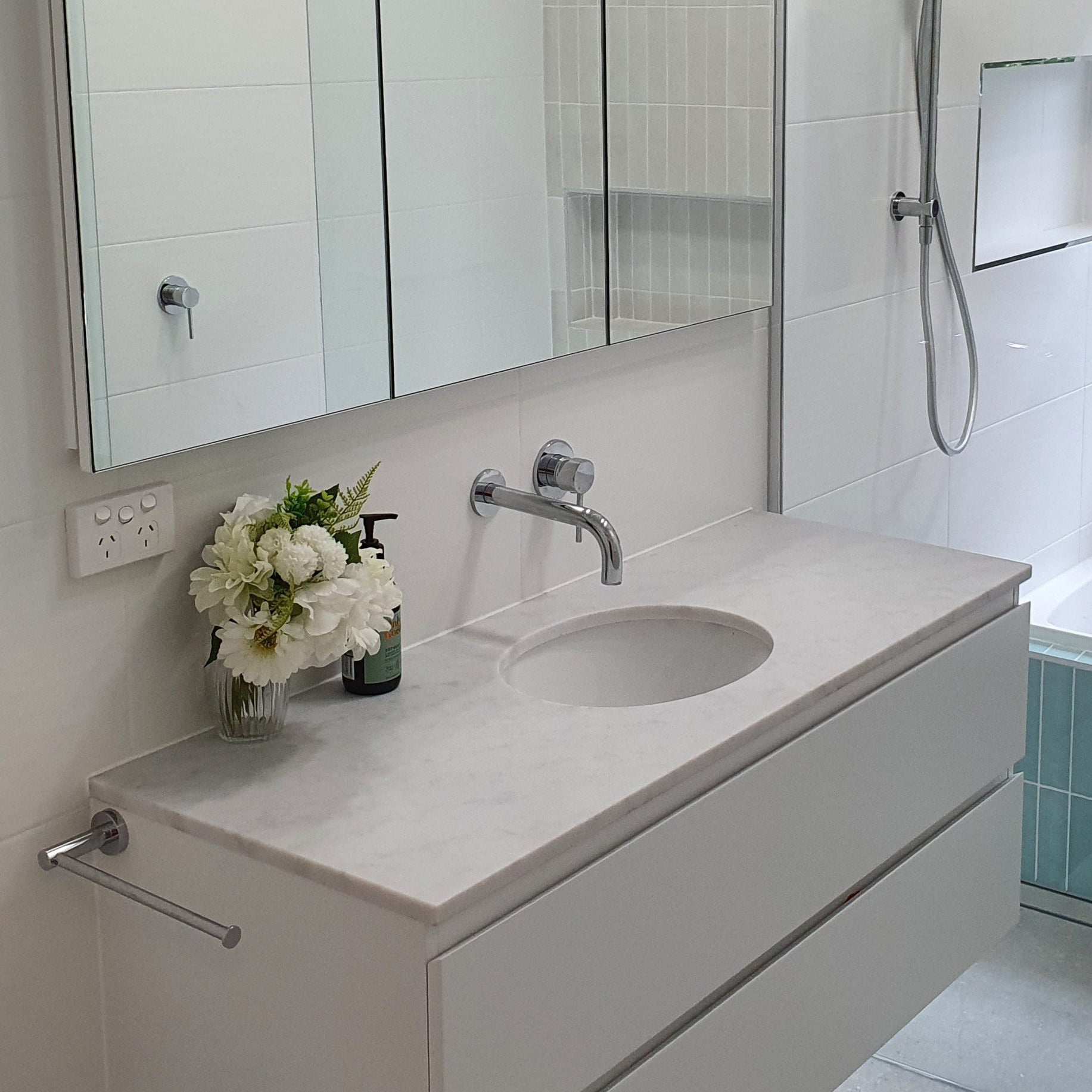 Modern bathroom with chrome towel holder, spout and mixer with a white vanity, sink, and bathtub.