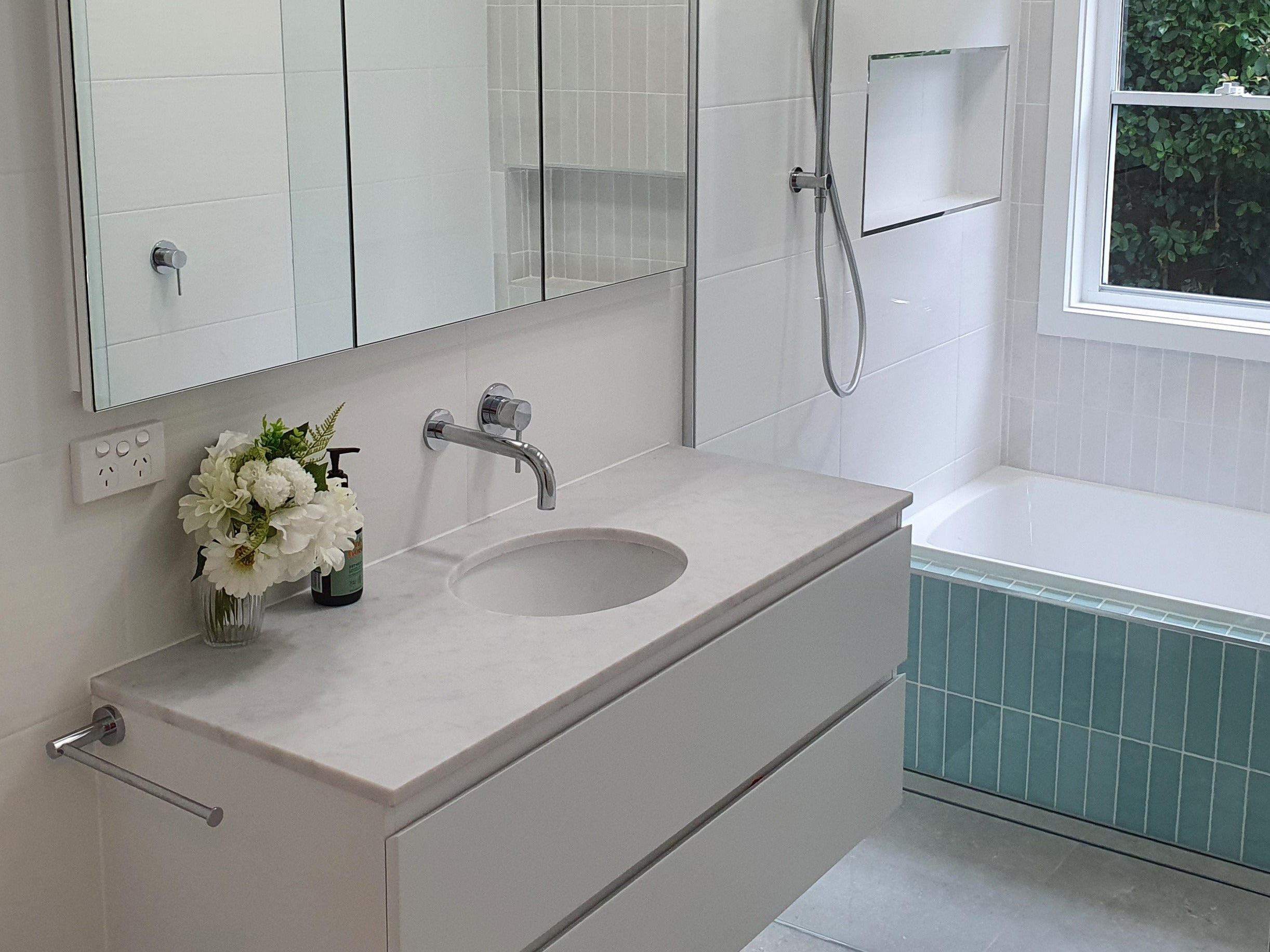 Modern bathroom with chrome towel holder, spout and mixer with a white vanity, sink, and bathtub.