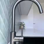 Gun metal kitchen/laundry mixer in a modern laundry setting with green tiles and a plant.