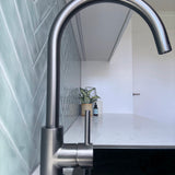 Gun metal kitchen/laundry mixer in a modern laundry setting with green tiles and a plant.