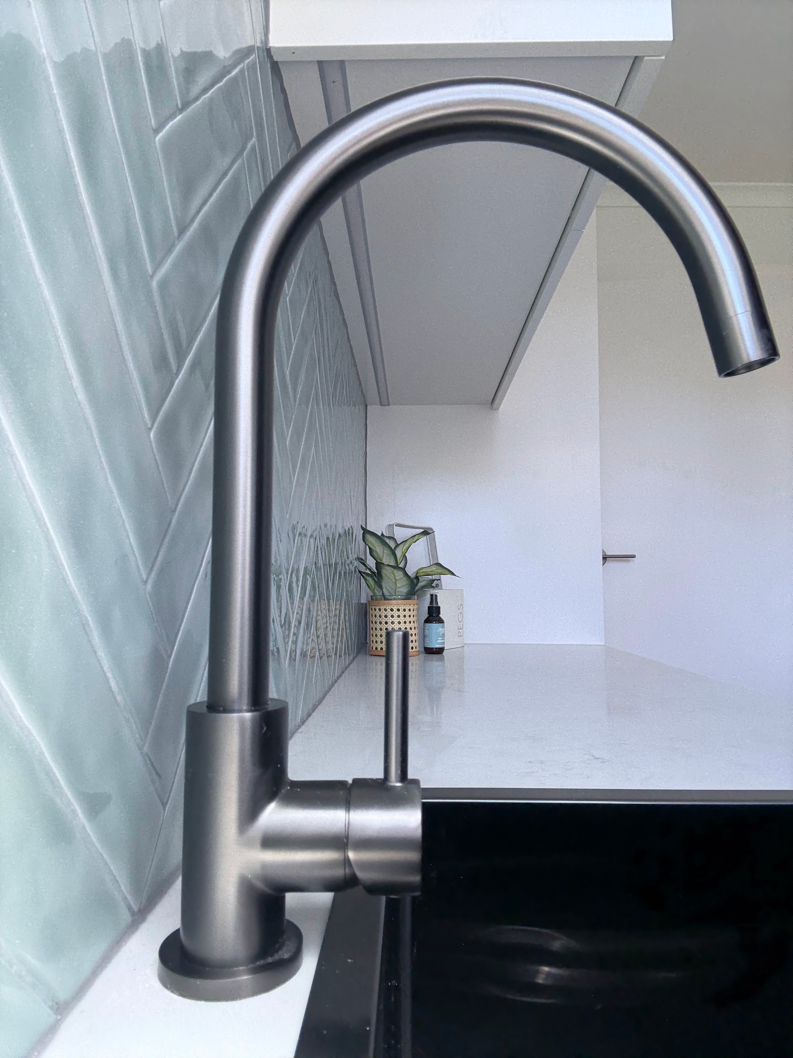 Gun metal kitchen/laundry mixer in a modern laundry setting with green tiles and a plant.