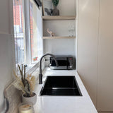 Modern kitchen with white countertops, black sink, and gun metal pull out kitchen/laundry mixer.