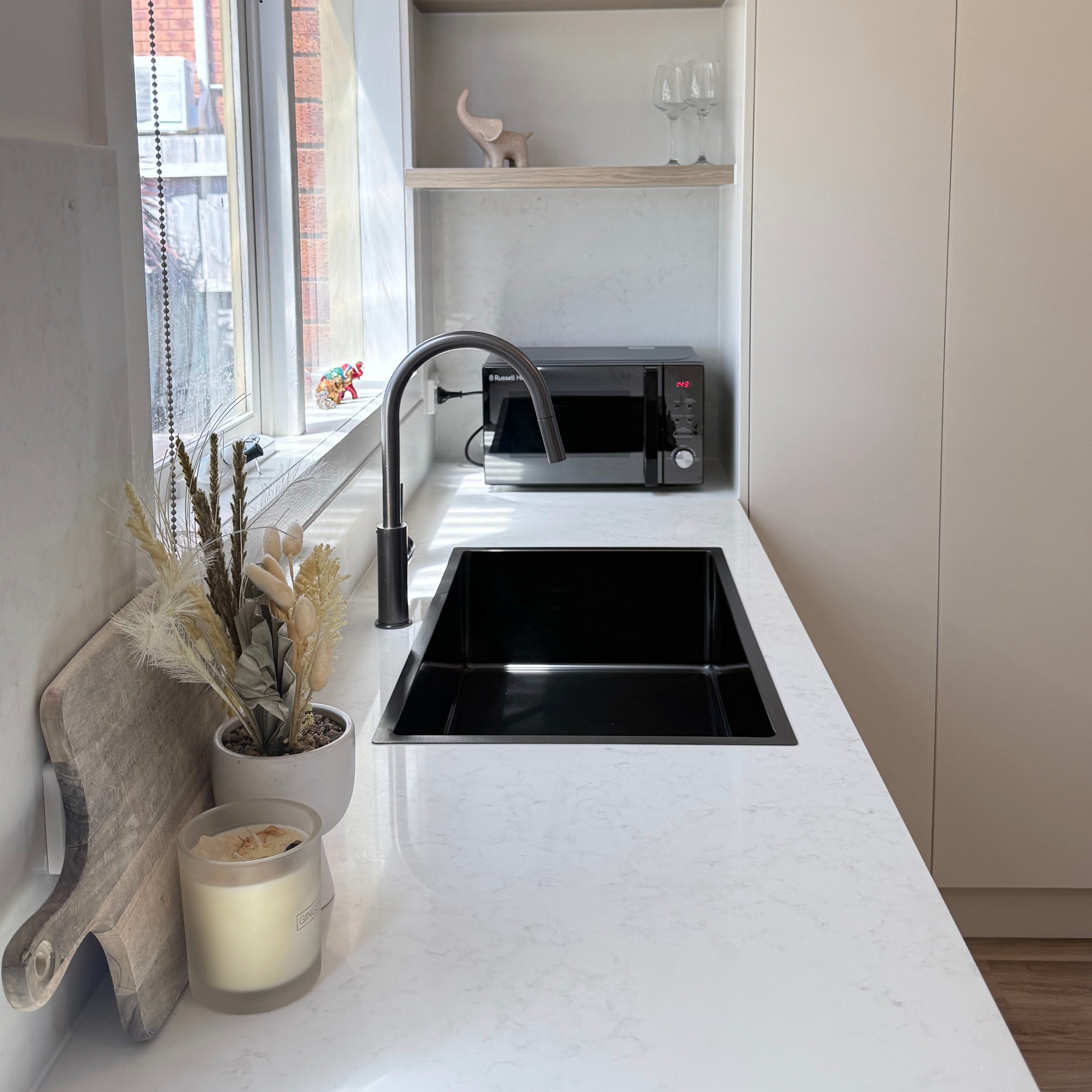 Modern kitchen with white countertops, black sink, and gun metal pull out kitchen/laundry mixer.