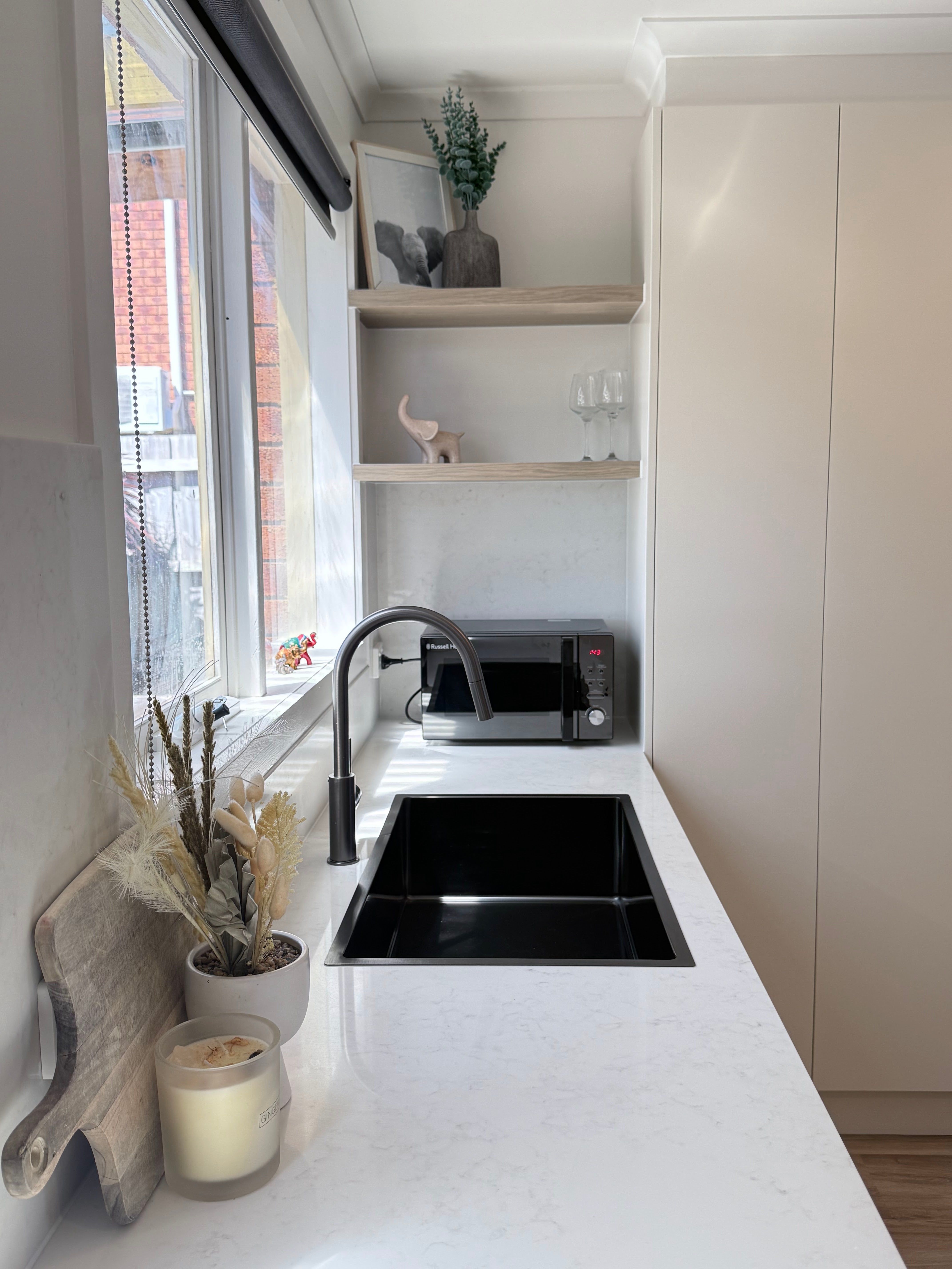 Modern kitchen with white countertops, black sink, and gun metal pull out kitchen/laundry mixer.