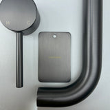 Gun Metal bathroom fixtures including a sample disc, wall mixer and wall spout  on a grey background.