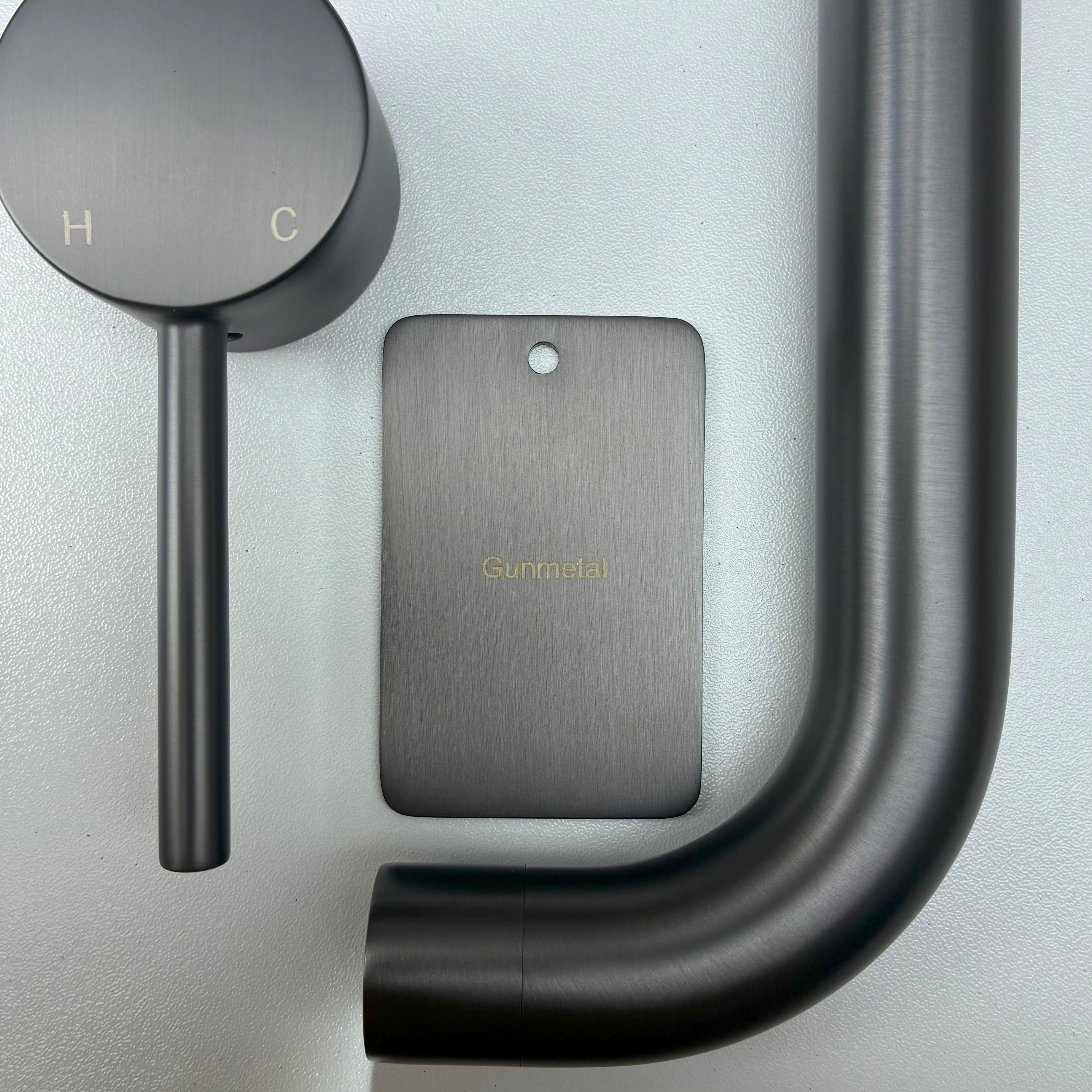Gun Metal bathroom fixtures including a sample disc, wall mixer and wall spout  on a grey background.
