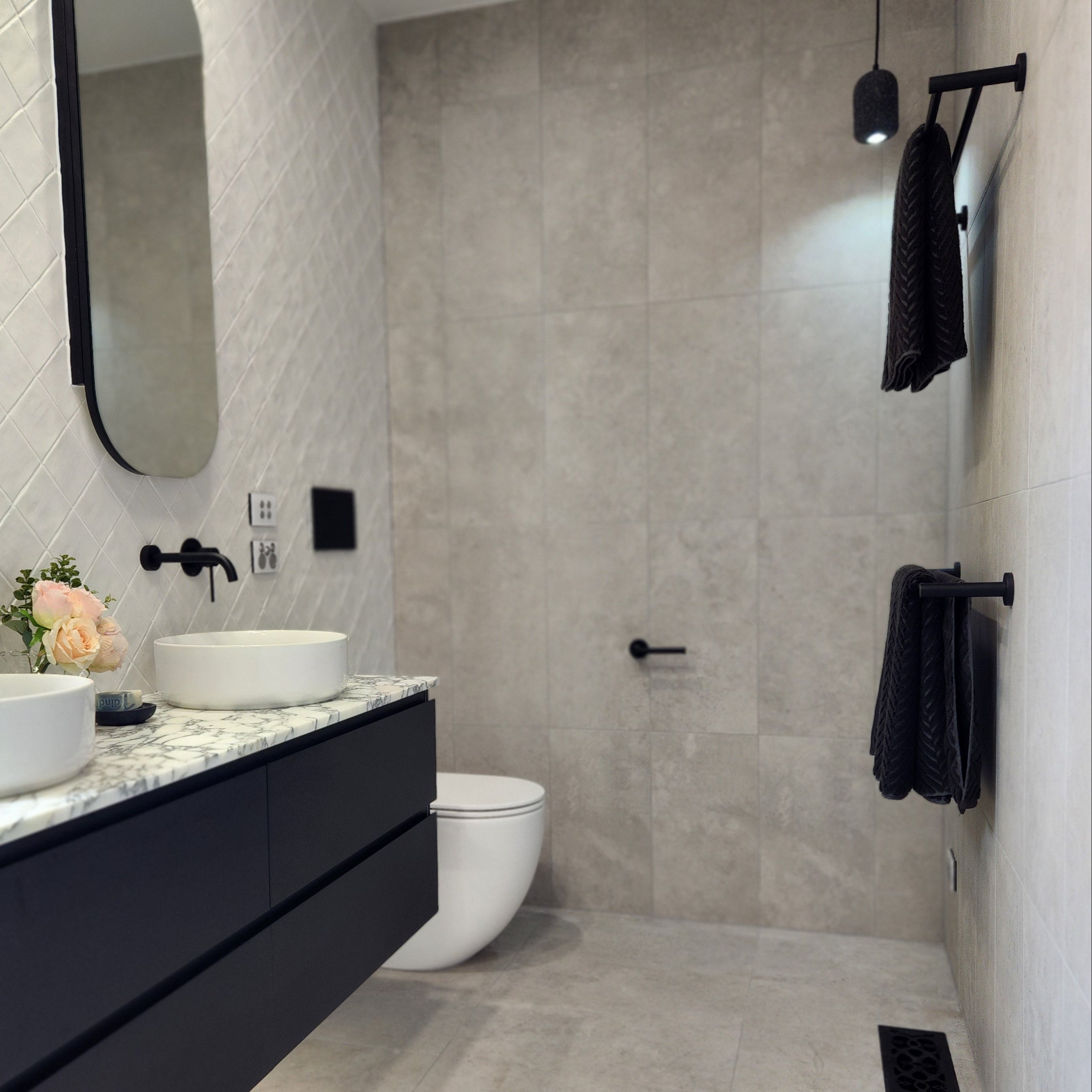 a set of matt black double towel rails wall mounted in modern bathroom interior with grey tiles, a bathtub, and a sink.
