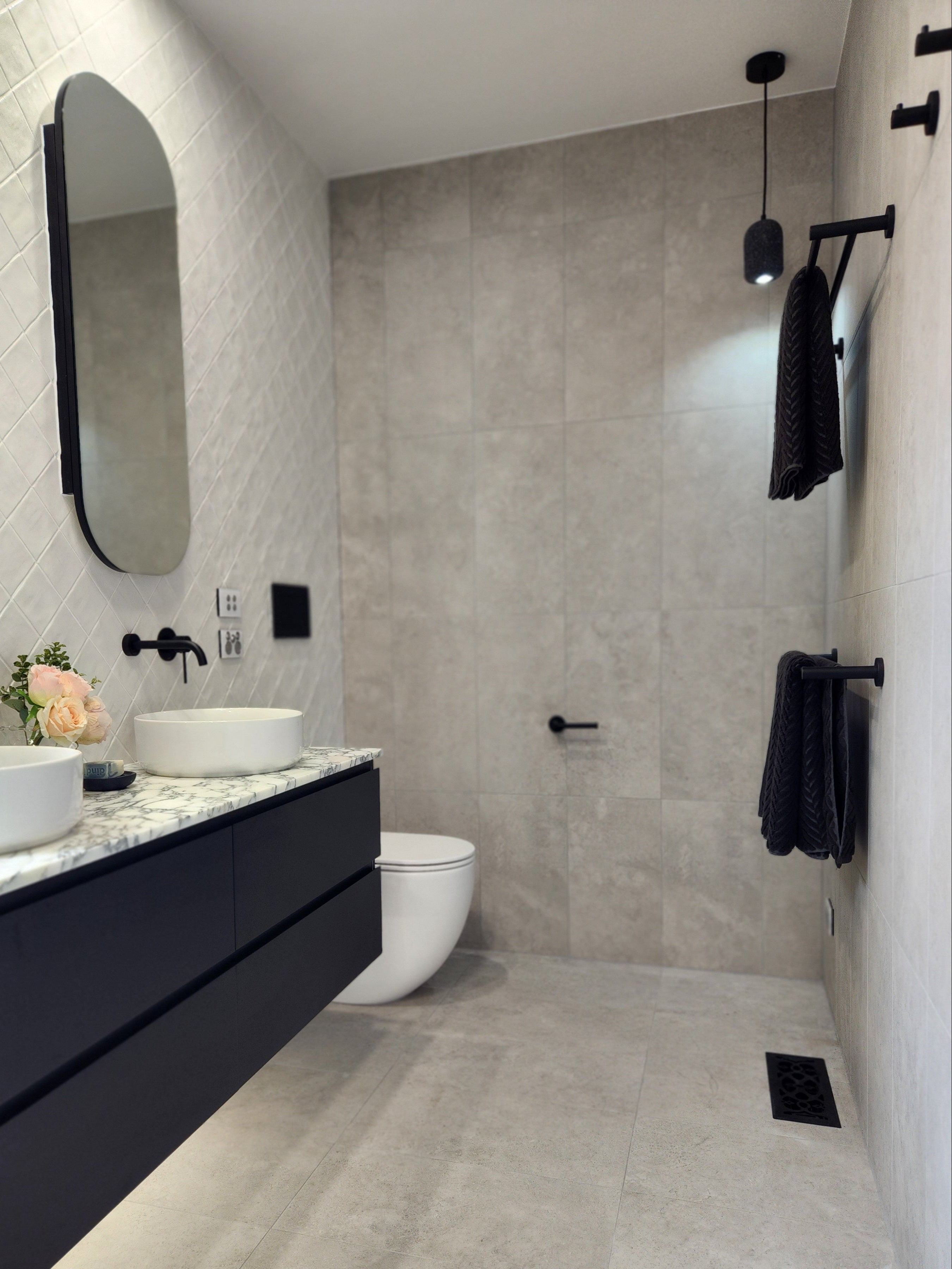 a set of matt black double towel rails wall mounted in modern bathroom interior with grey tiles, a bathtub, and a sink.