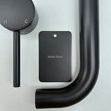 Matt black bathroom fixtures including a sample disc, wall mixer and wall spout  on a grey background.
