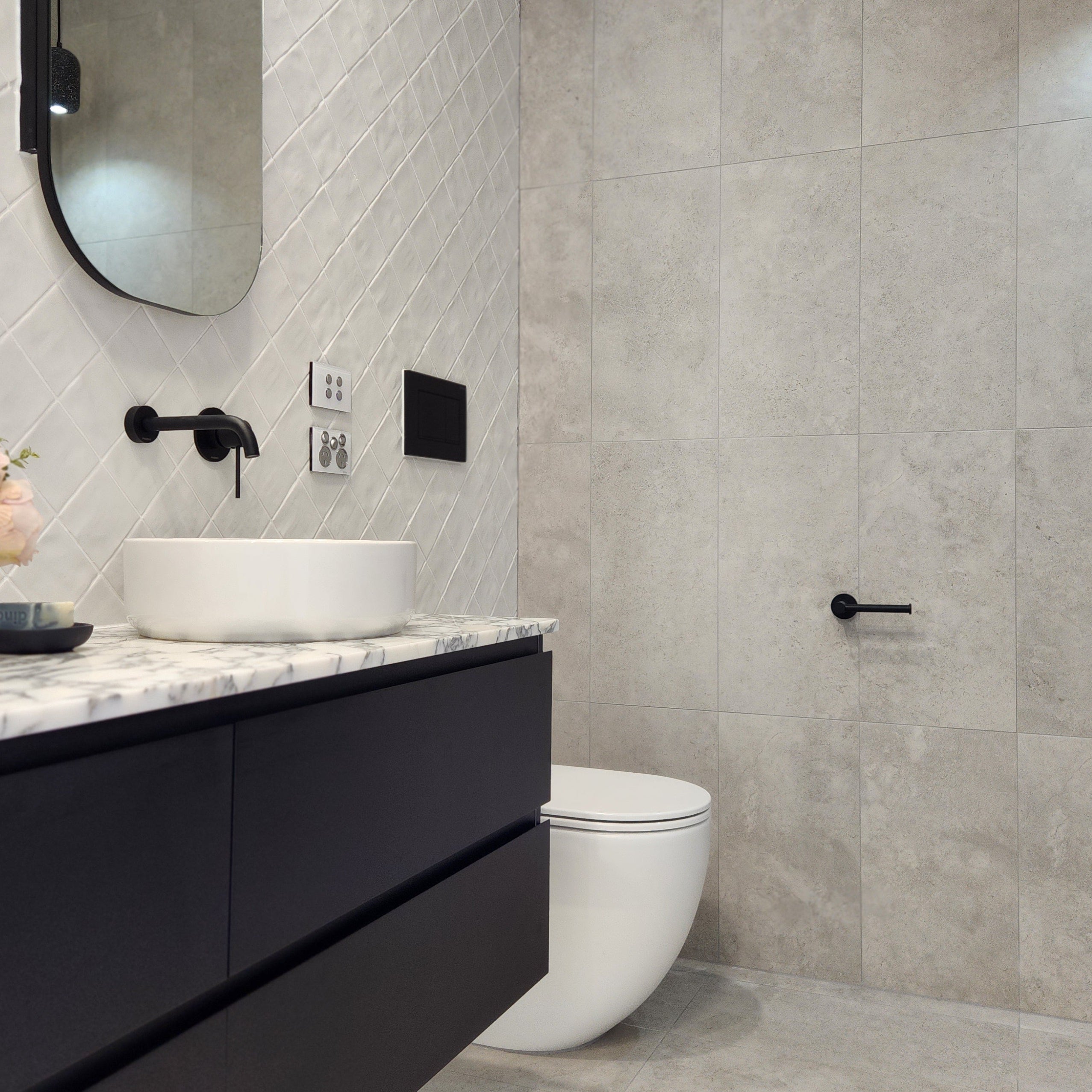 an matt black toilet roll holder in a modern bathroom with black vanity, white sink, and toilet.