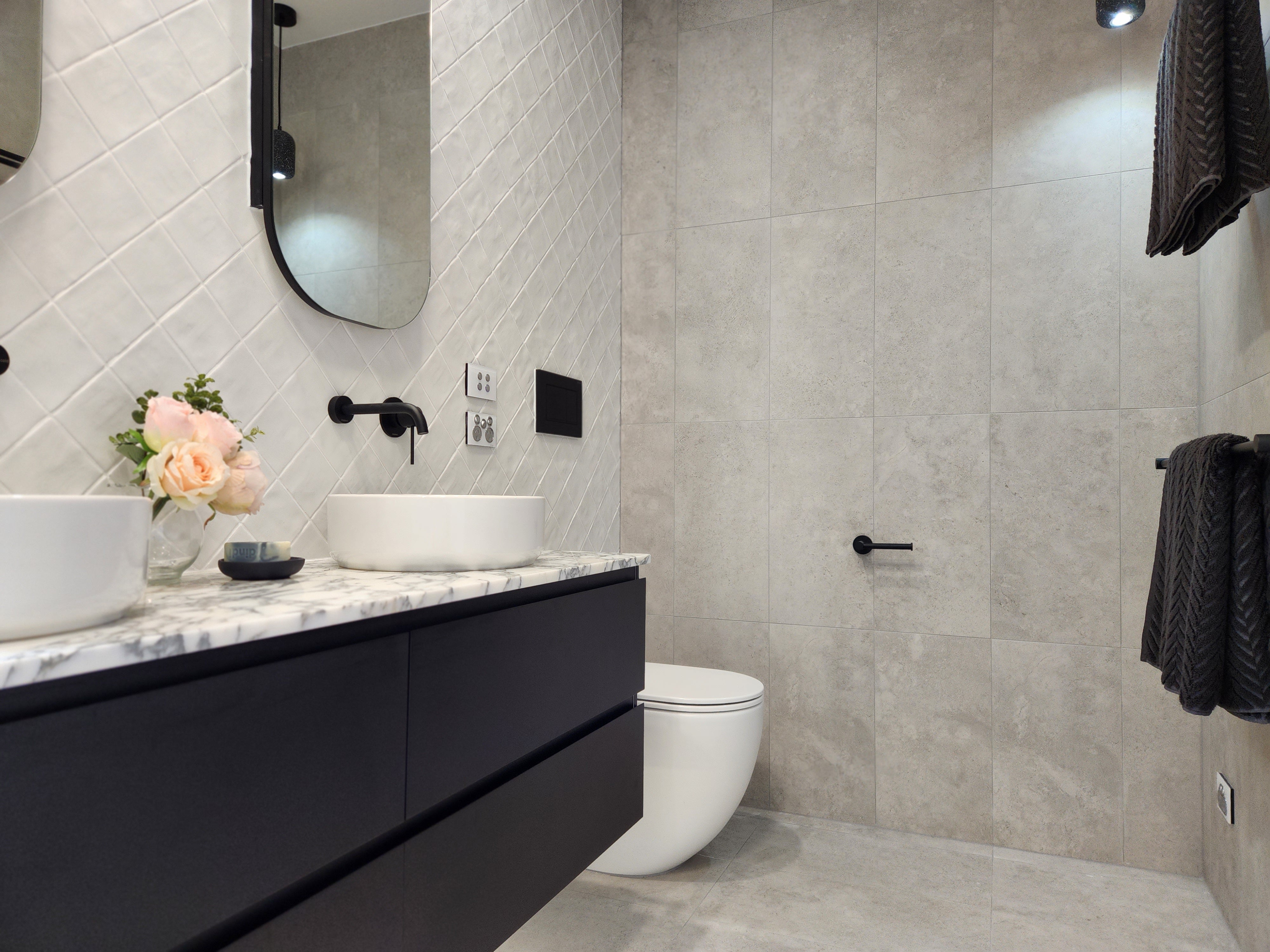 an matt black toilet roll holder in a modern bathroom with black vanity, white sink, and toilet.