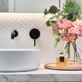 a matt black wall mixer and spout on a white tiled background