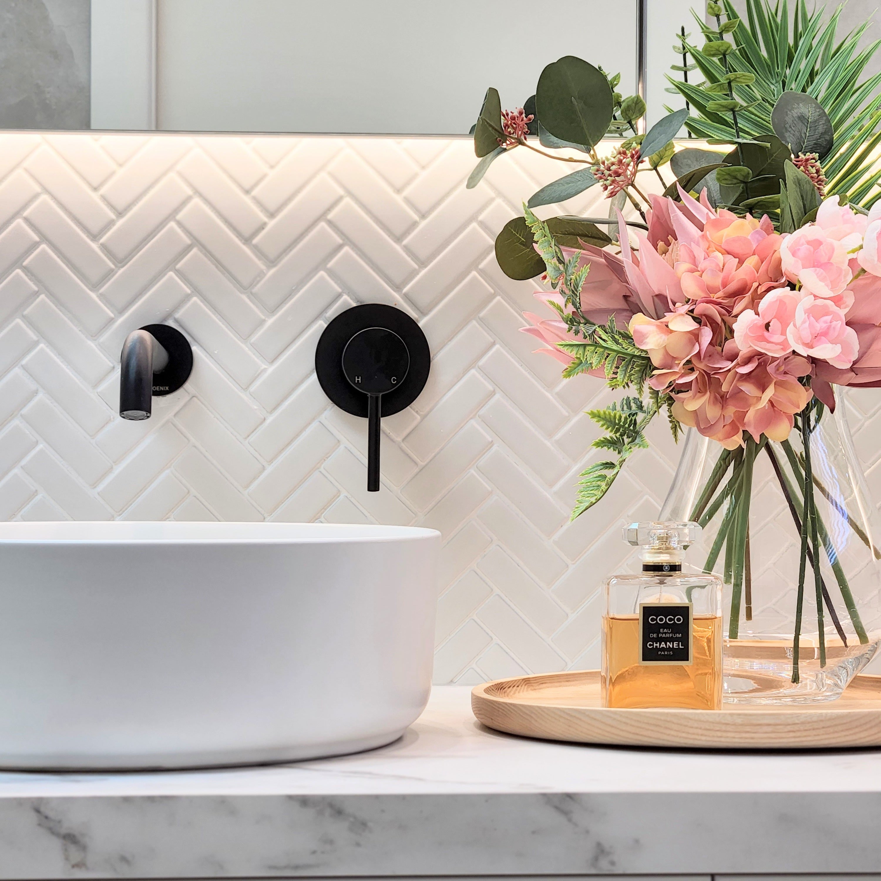a matt black wall mixer and spout on a white tiled background
