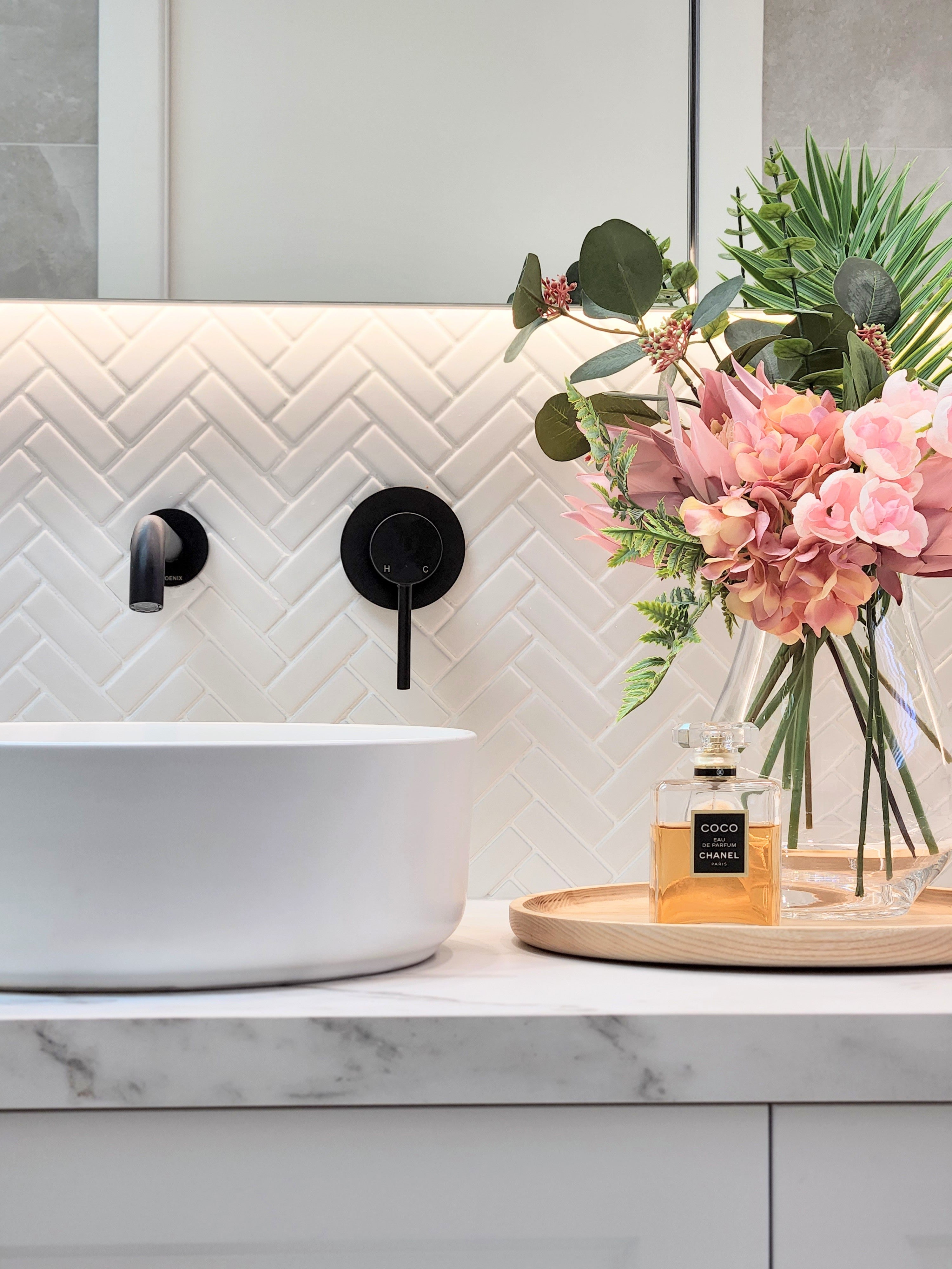 a matt black wall mixer and spout on a white tiled background