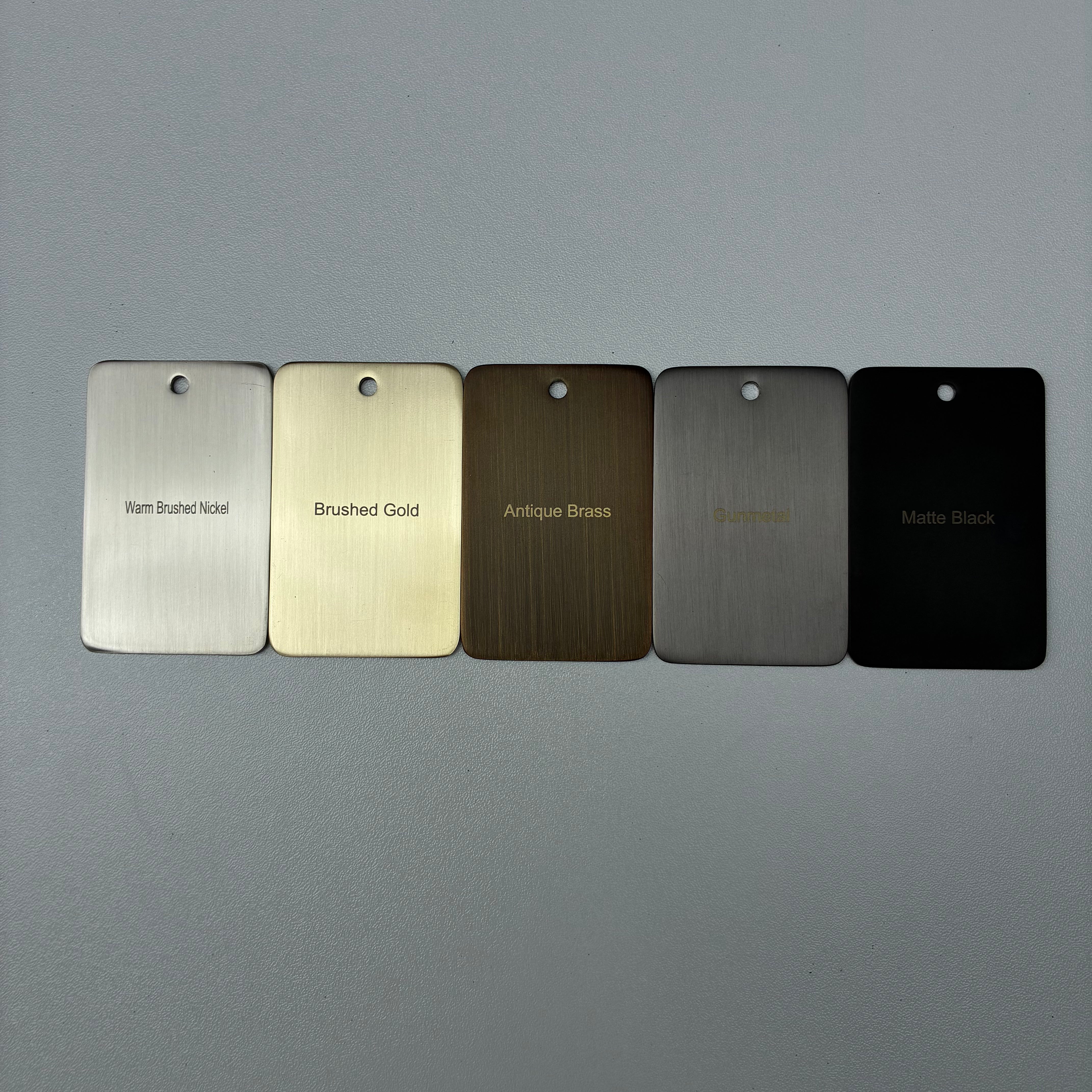 Five metal color samples labeled 'Warm Brushed Nickel', 'Brushed Gold', 'Antique Brass', 'Gun Metal', and 'Matt Black' on a grey background. 