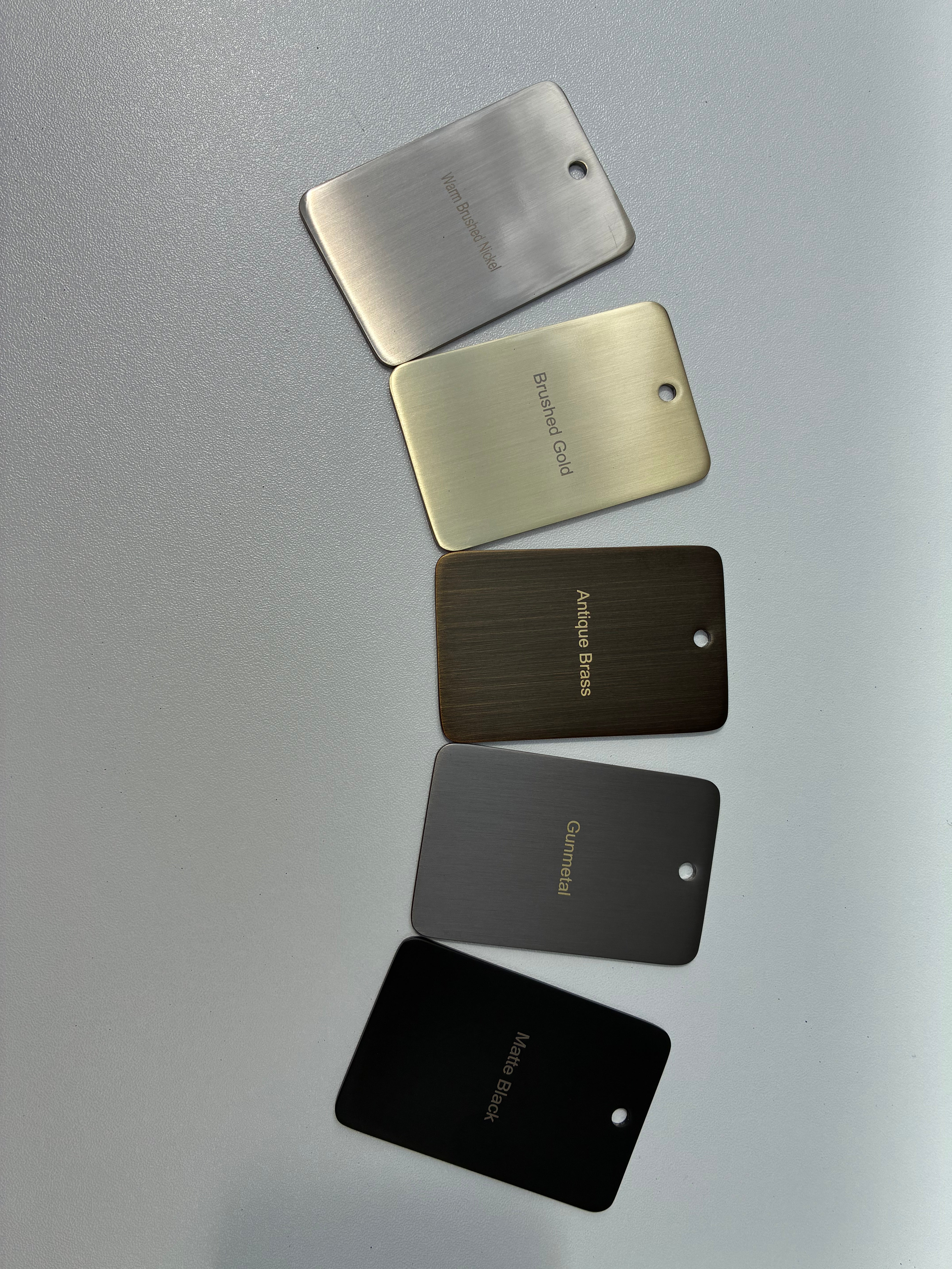 Five metal color samples labeled 'Warm Brushed Nickel', 'Brushed Gold', 'Antique Brass', 'Gun Metal', and 'Matt Black' on a grey background.